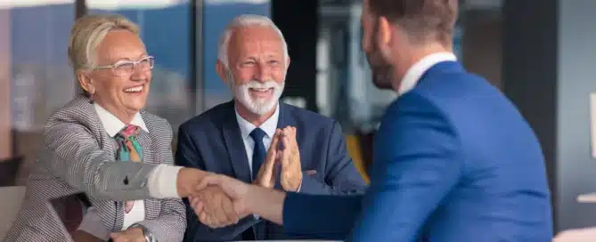 Business owners shaking hands with a financial advisor while discussing the benefits of using an SBA loan to purchase an existing business.