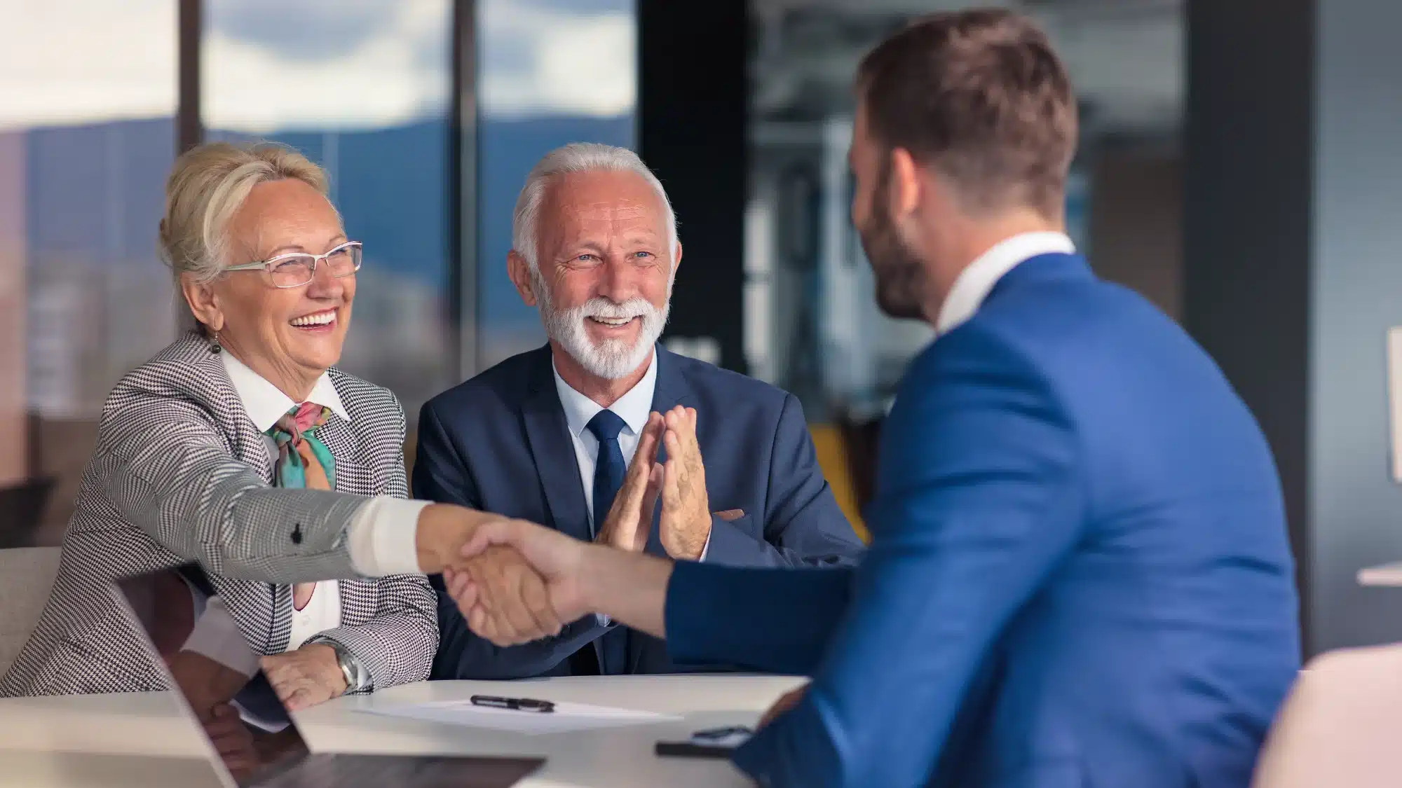 Business owners shaking hands with a financial advisor while discussing the benefits of using an SBA loan to purchase an existing business.